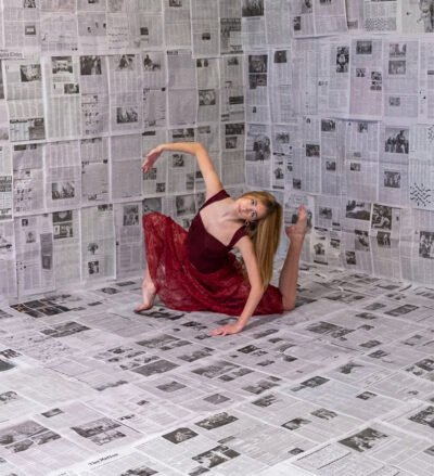 Young teen girl posing in a ballet position with newspapers in the background.